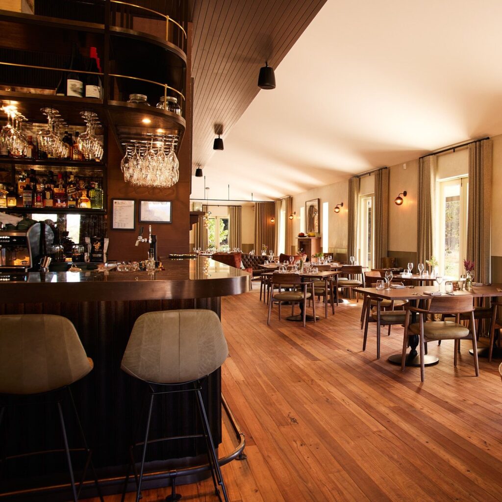 A stylish, modern restaurant with wooden floors, neatly set tables, and cushioned chairs offers one of the best experiences in the Blue Mountains. Large windows fill the curved bar area with inviting natural light. | Werriberri